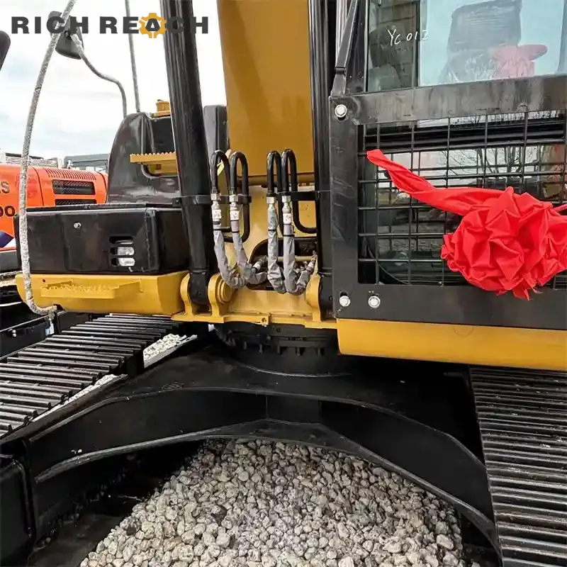 Close-up view of hydraulic hoses with protective sleeves, boom cylinder bases, and slewing ring on a Caterpillar 320D2 excavator.