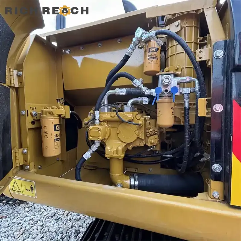 Detailed interior view of a Caterpillar excavator hydraulic pump compartment, featuring the main pump, multiple Cat filters, and high-pressure hoses.
