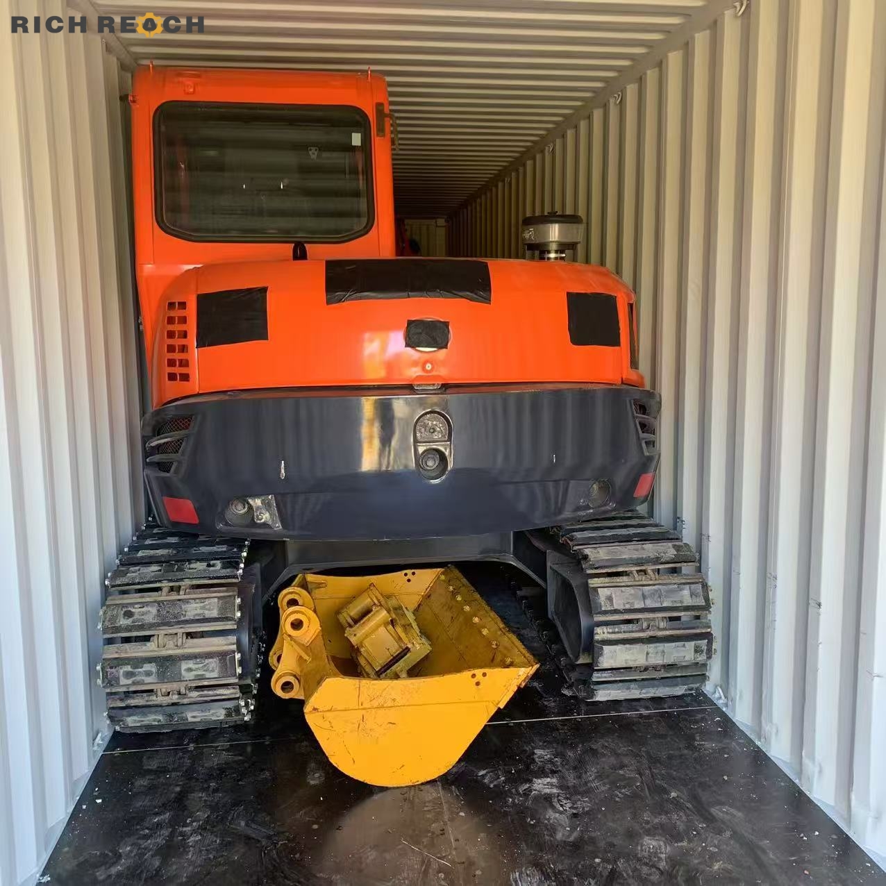 An orange crawler excavator and its detached yellow bucket carefully loaded inside a standard ocean shipping container for global transport.